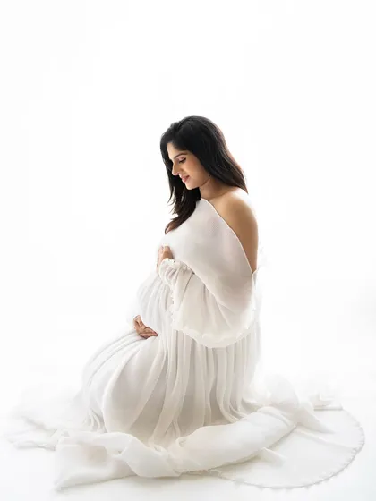 A serene kneeling pose, with the soft white gown pooling around her. This pose is wonderful for highlighting the beautiful shape of the baby bump.