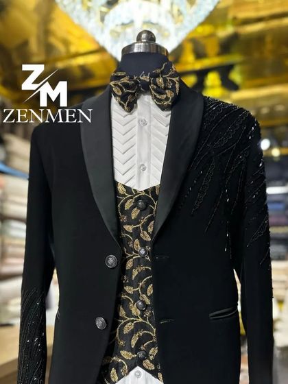 A black tuxedo with a unique gold-patterned waistcoat and bow tie. The jacket sleeves are embellished with black beads for a subtle, textured finish.