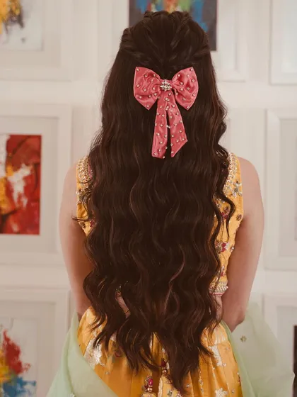 A cute and playful half-updo with soft waves, finished with a large pink bow. This is a great hairstyle for a fun daytime event or for the bride's sister.