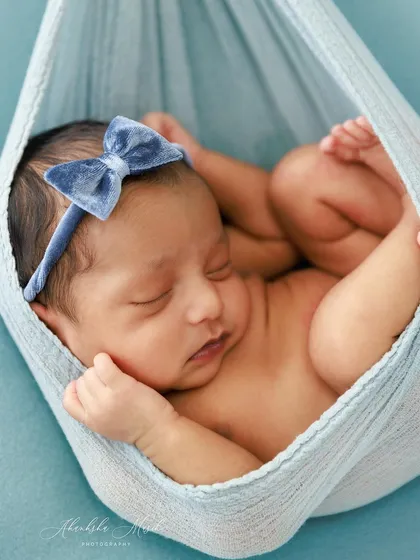 Gently cradled in a soft blue sling, this newborn is in a classic and safe "womb" pose. The monochromatic color scheme creates a calm and soothing visual, highlighting the baby's peaceful slumber.