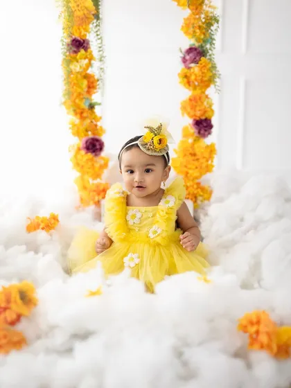 A dreamy first birthday setup with a baby girl in a yellow dress, sitting on a cloud with a floral swing. We create magical sets to make their first birthday unforgettable.