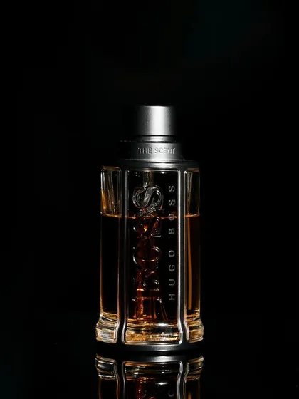 A minimalist and classic luxury product shot. By placing the bottle on a reflective black surface against a pure black background, all attention is drawn to the product's shape and branding. This low-key lighting technique is effective for creating a sophisticated and premium feel.