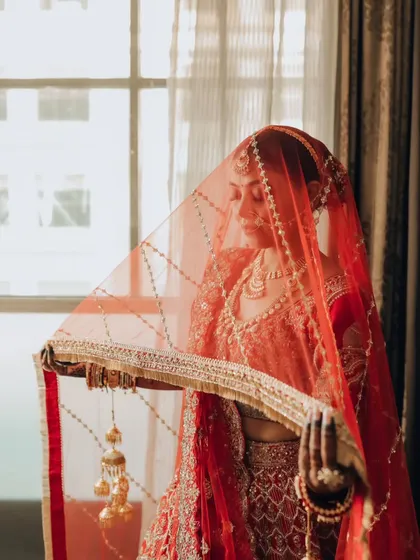 A classic bridal portrait with the veil. The soft red light and her gentle expression create an aura of timeless beauty.