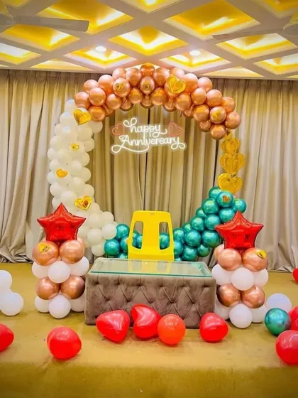 A colorful anniversary backdrop with a circular balloon arch in multiple colors. The setup includes a neon sign and is designed to fit around existing furniture for a home party.