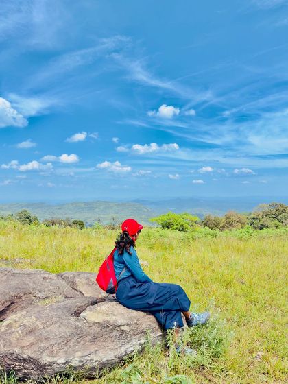 A trekker with a red backpack sits on a rock, providing a nice color contrast.