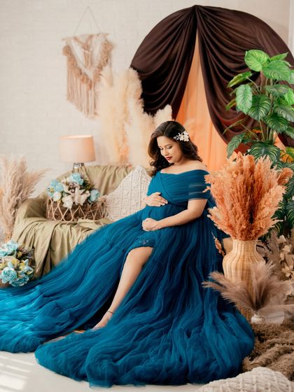 A dreamy, boho-chic setup featuring a mom-to-be in a magnificent blue tulle gown. The pampas grass, soft lighting, and layers of fabric create a whimsical and romantic feel.