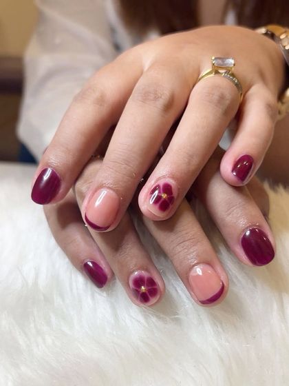 Blooming flowers on natural nails. This design features a deep pink shade with accent nails showing a sheer base and a hand-painted blooming flower.