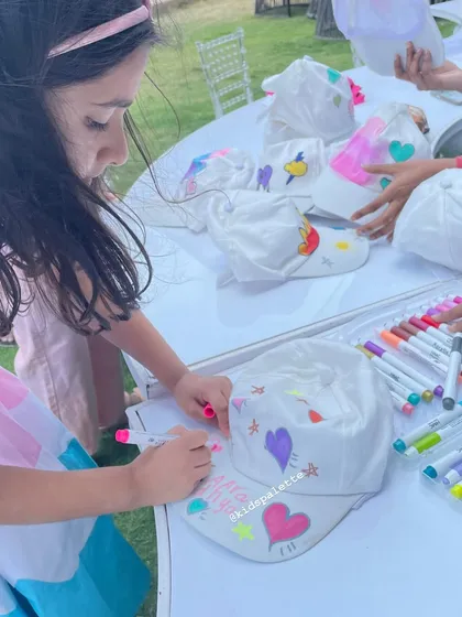 This young guest is carefully adding her name and some stars to her cap. Wearable art activities help build confidence and a sense of ownership.