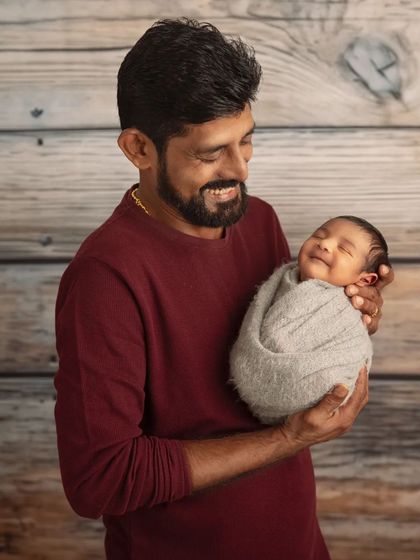 A father's gentle hold. This portrait captures the pure joy on a new dad's face as he cradles his smiling, swaddled newborn.