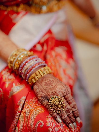 A close-up focusing on the bride's hand, her traditional ring, and the beautiful mehendi stain against her red silk saree.
