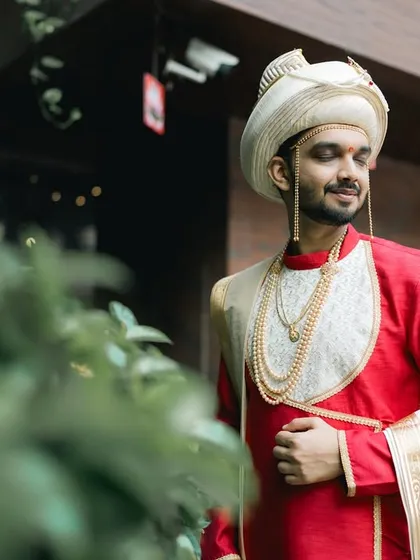 A portrait of a Maharashtrian groom in a striking red and white outfit, looking regal and ready.