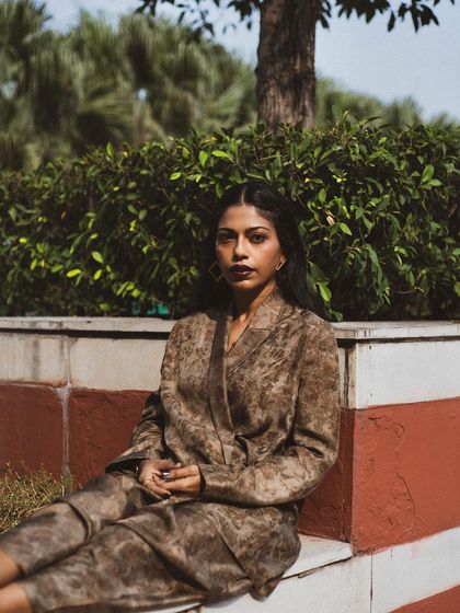 A seated portrait of Anasuya Sengupta, conveying a sense of calm and confidence. The natural setting provides a soft, beautiful backdrop.