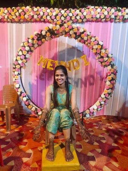 The bride is ready for her mehndi ceremony. Here she is, sitting against a beautiful floral backdrop, with her hands and feet fully decorated with my intricate henna designs.