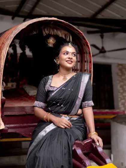 A full-length shot of the model in a black saree, seated in a traditional palanquin. The entire look is a beautiful blend of tradition and modern elegance.