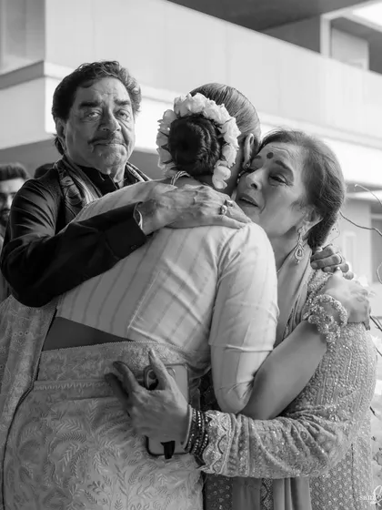 A graceful bride hugs her emotional mother, as her father stands tall beside them. This family hug is a powerful tableau of love, support, and the bittersweet emotions of a wedding day.
