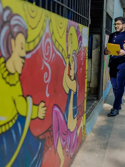 The groom walks outside the registrar's office, documents in hand, against a colorful mural.