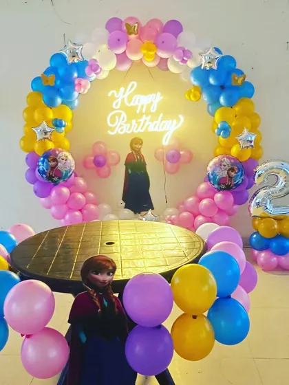 A Frozen-themed second birthday party. The setup features a balloon ring in Elsa's colors, character cutouts, and a silver foil number '2' for the birthday girl.
