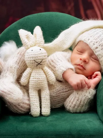 A newborn dressed as a bunny sleeps on a miniature green sofa with a crochet bunny prop. An adorable and creative setup.