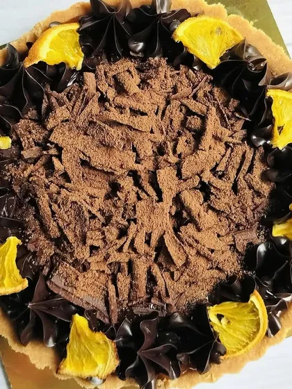 A top-down view of the dark chocolate orange tart, showcasing the rustic texture of the chocolate shavings and the bright pop of color from the orange slices.
