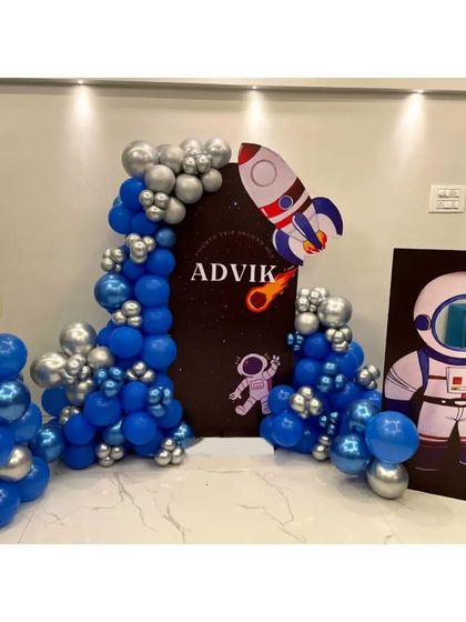 A closer look at our space-themed party decor, featuring a personalized backdrop for "Advik". The setup includes a fun astronaut photo-op cutout and a blue and silver balloon arch that mimics the night sky.