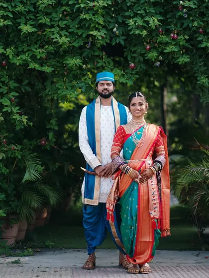 A formal portrait of the couple in their stunning Marathi wedding attire. The rich colors and intricate details are captured against a backdrop of natural greenery.