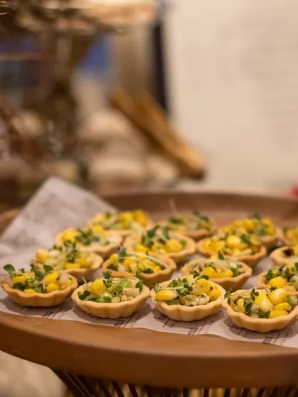 A close-up of our mini corn tarts, a delightful and savory bite-sized treat. The presentation on a wooden platter adds a rustic yet chic touch to the canapé service.