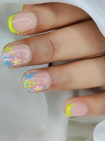 A close-up of a playful floral design on short nails. The combination of a neon yellow French tip and tiny pastel flowers is perfect for summer.