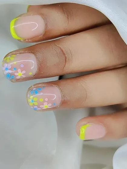 A close-up of a playful floral design on short nails. The combination of a neon yellow French tip and tiny pastel flowers is perfect for summer.
