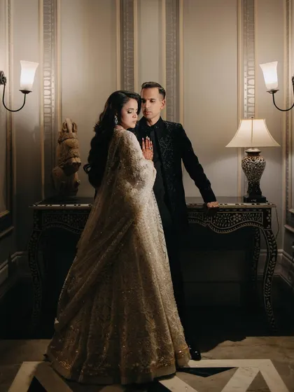A full-length portrait in a classically decorated hallway. The warm ambient light and their elegant poses give this shot a timeless, old-world glamour.