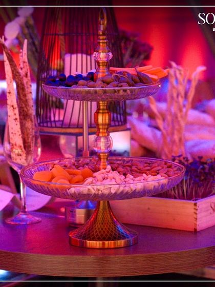 A sophisticated setup for a victory celebration, featuring a tiered stand with dry fruits and nuts under dramatic red lighting. We curate the perfect ambiance for every type of social gathering.