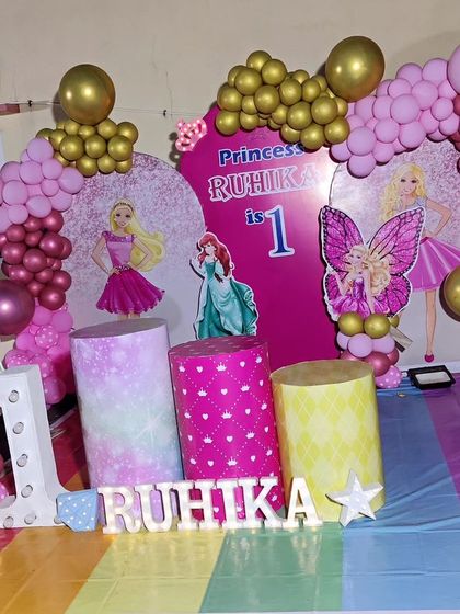 A full-stage princess-themed first birthday. The decor includes a rainbow-colored floor, princess cutouts, and a large light-up number '1'.