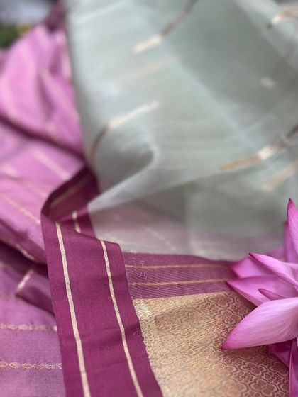 The ethereal quality of Tissue Silk. This saree combines a pastel green body with a vibrant pink and gold border, creating a piece that is both lightweight and visually stunning.