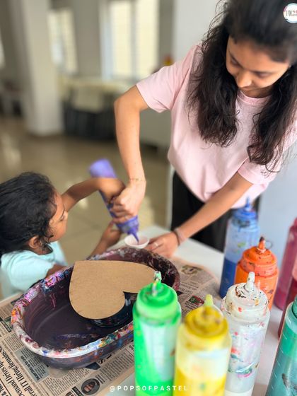 Teamwork makes the dream work. A young girl gets a little help pouring paint onto her heart-shaped canvas, a perfect activity for siblings or friends.
