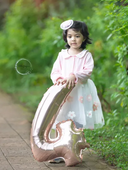 Four and flourishing. This portrait captures the sweet innocence of a four-year-old during her milestone photoshoot, complete with a pretty dress and a matching number balloon.