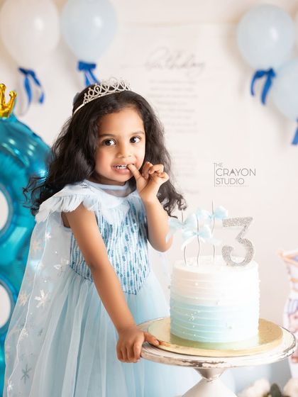 A little princess, dressed as Elsa, tentatively tastes her third birthday cake. A sweet and shy moment.