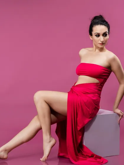 A graceful portrait in a flowing red dress against a solid pink background. The color contrast and elegant pose create a visually stunning image perfect for editorial fashion.