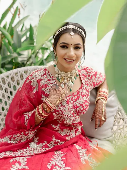 A beautiful portrait of the bride seated, looking serene and happy. The makeup is flawless, and her red lehenga looks absolutely stunning.