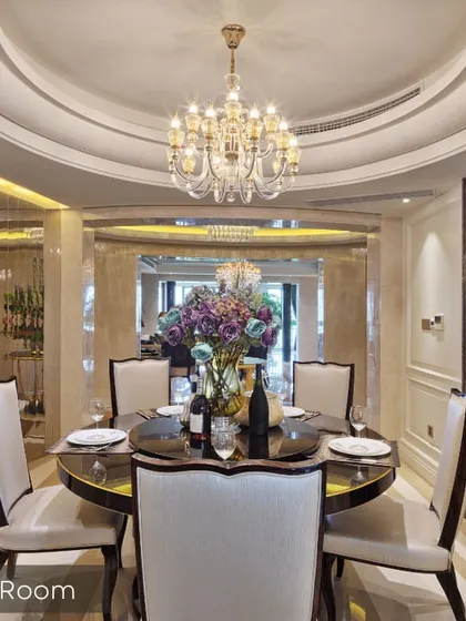 An elegant dining room setup featuring a round table, a stunning crystal chandelier, and a coffered ceiling design. The space is perfect for intimate family dinners and hosting guests.