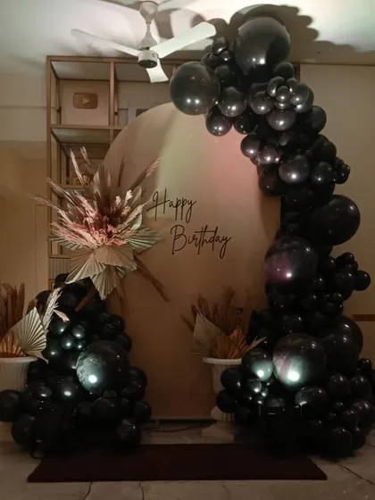 A sophisticated and moody birthday decoration for a home setting, using a black balloon arch and dried pampas grass for a modern, masculine feel.