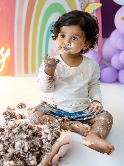 A sweet portrait of the baby looking up, with frosting on her face, amidst the colorful birthday setup.