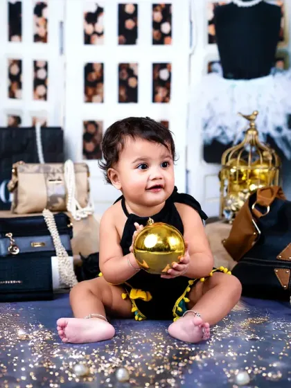 A baby boy joins the stylish fun, sitting among the glamorous props and holding a golden ball.