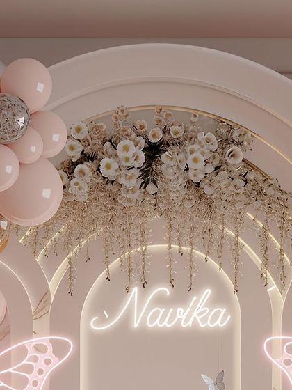 A custom neon sign with the birthday girl's name, 'Navika', serves as a beautiful focal point. Set against a backdrop of cascading white flowers and a pastel arch, it makes the celebration feel truly personal.