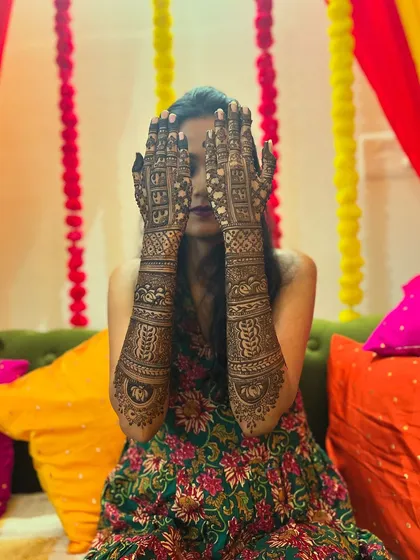 A classic mehendi pose, with the bride hiding her face behind her beautifully decorated hands.