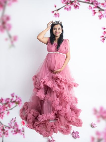 A queen and her bump. Wearing a crown and a gorgeous pink gown, this mom-to-be looks absolutely radiant and happy in this floral-themed portrait.
