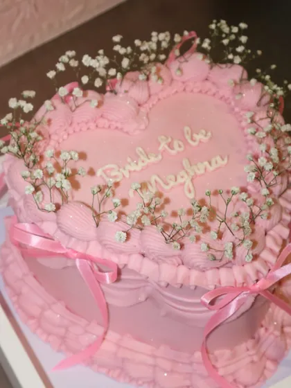 A dreamy bridal shower cake for the "Bride to be." This all-pink, heart-shaped vintage cake is adorned with delicate piping, ribbons, and sprigs of baby's breath.