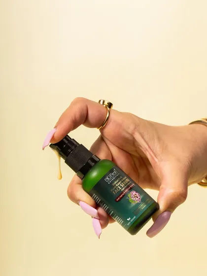 A dynamic shot of a hand dispensing a drop of Biofresh Botanicals' face serum. This action shot is engaging and highlights the product's texture and color.