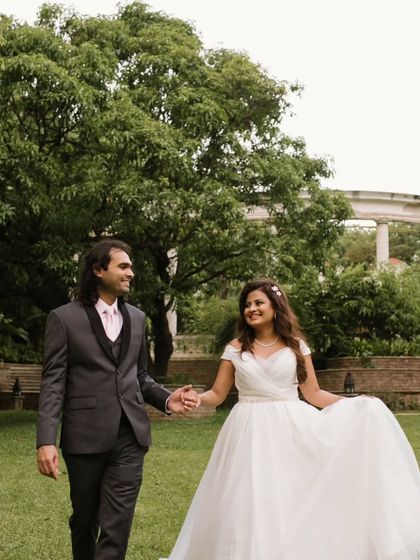 The bride and groom take a romantic walk through a lush green park after their wedding, holding hands and sharing a smile.