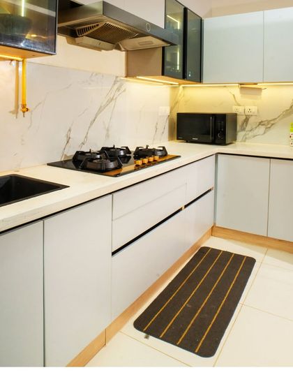 The kitchen at Brigade Cornerstone Utopia, featuring light grey handleless cabinets, a white marble-patterned backsplash, and integrated under-cabinet lighting.