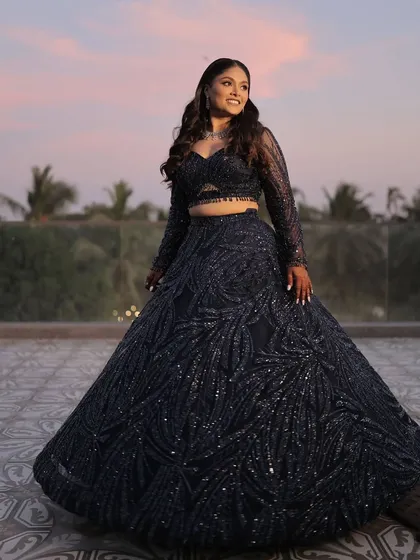 A full-length shot against a sunset sky. The deep blue of her lehenga and the pop of blue on her eyes create a stunning, cohesive look.