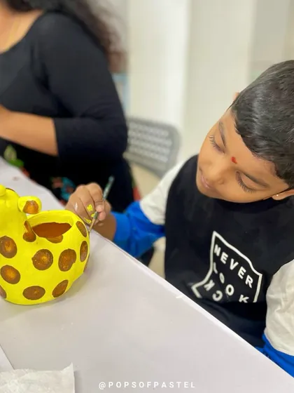 A young boy meticulously paints spots on his giraffe planter, showing great focus and creativity.